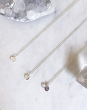 Three sterling silver cable necklaces placed on a marble board, all with an initial pendant and the third with a silver opal pendant
