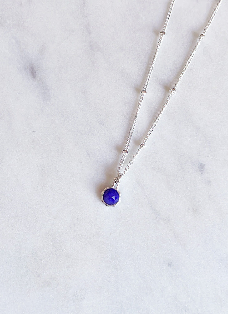 Silver necklace with a blue sapphire pendant and fancy dotted chain on a marble surface