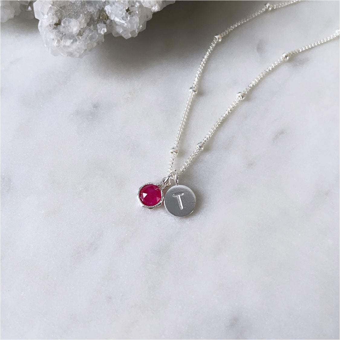 Personalised birthstone necklace with a round faceted ruby pendant and a sterling silver initial pendant