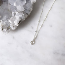 Round white topaz necklace in sterling silver on marble top next to a crystal quartz