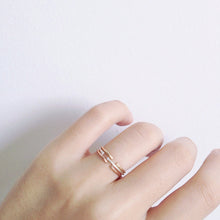 A hand wearing 3 dainty rings stacked together in gold, sterling silver and rose gold