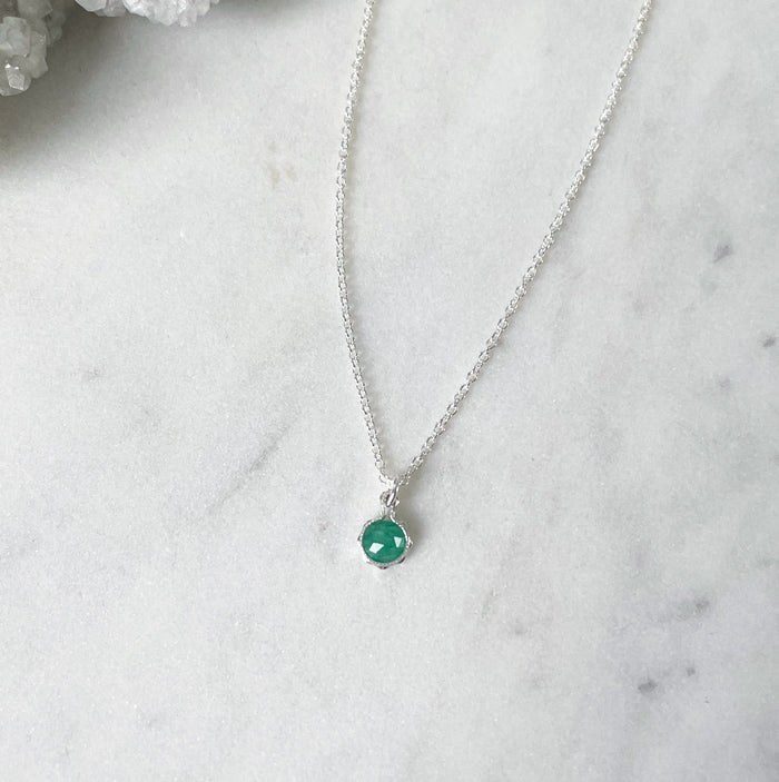 A faceted green emerald pendant in a sterling silver setting placed on a fine cable chain