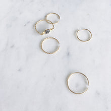 A collection of dainty fine gold rings, one with pavé set rough diamonds and others are open rings with a twisted and hammered finish