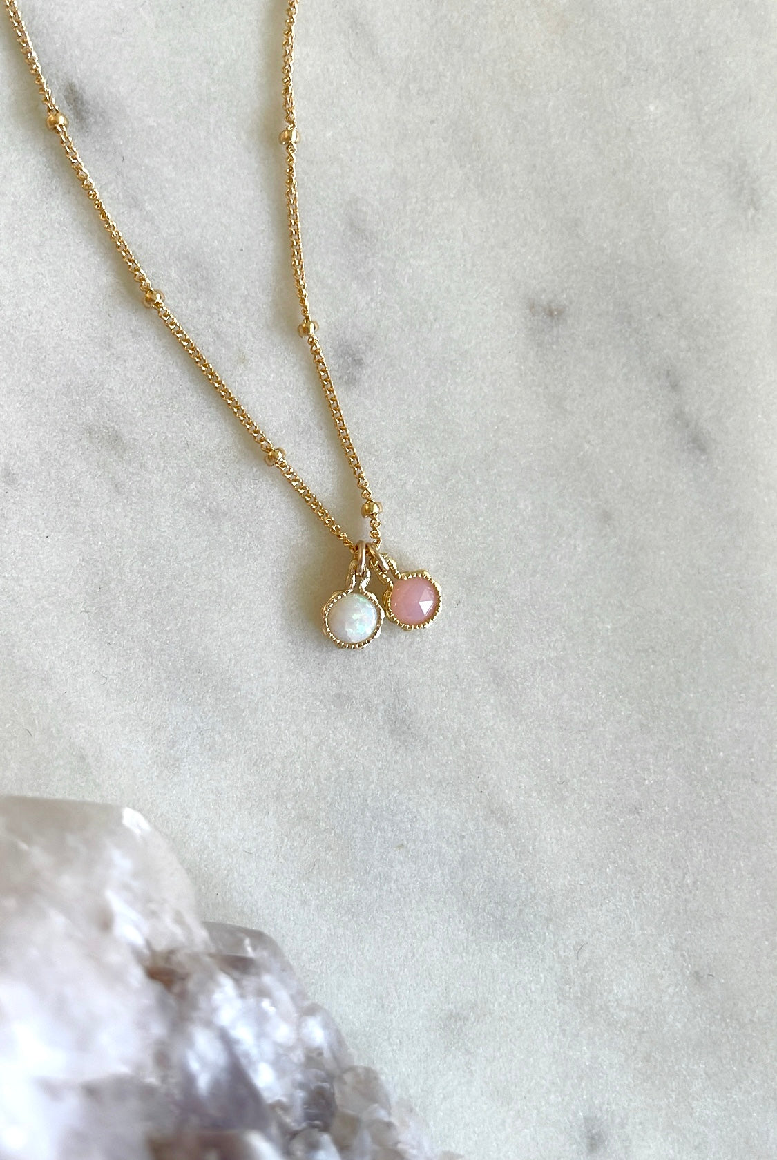 Gold october birthstone necklace with Australian opal and pink opal charm pendants on a marble surface