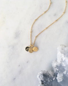 Personalised Gold initial necklace with 3 hand stamped letter pendants on a marble slab