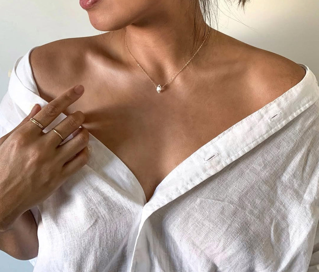 Woman wearing a white top and minimalist gold jewelry against a neutral background