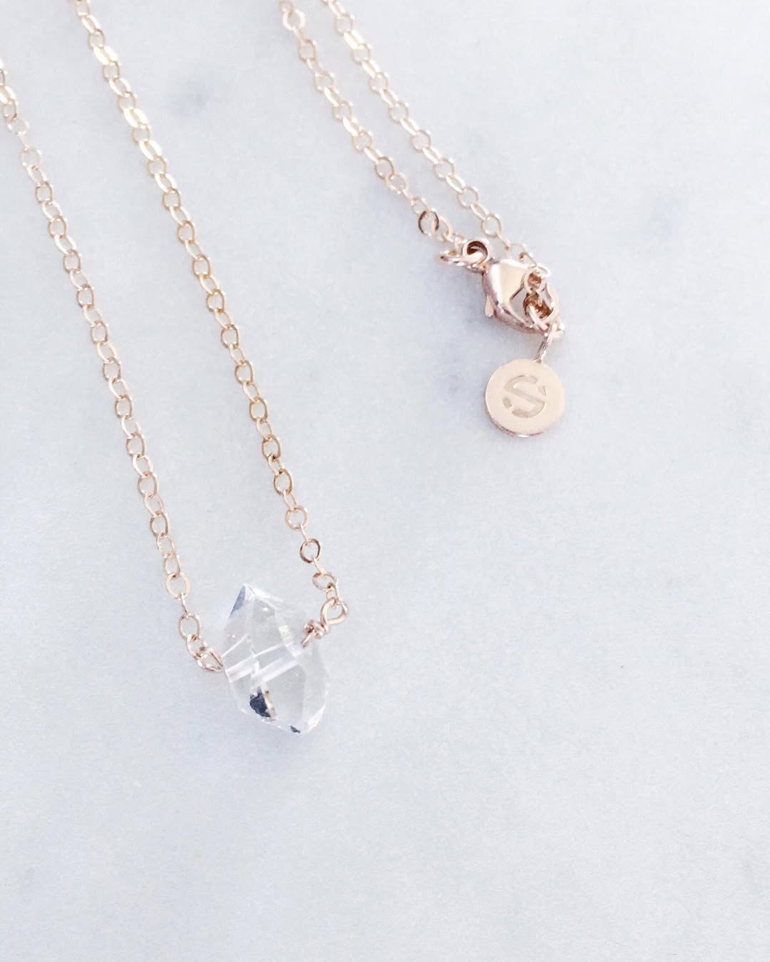 Gold necklace with a clear crystal pendant on a light grey background