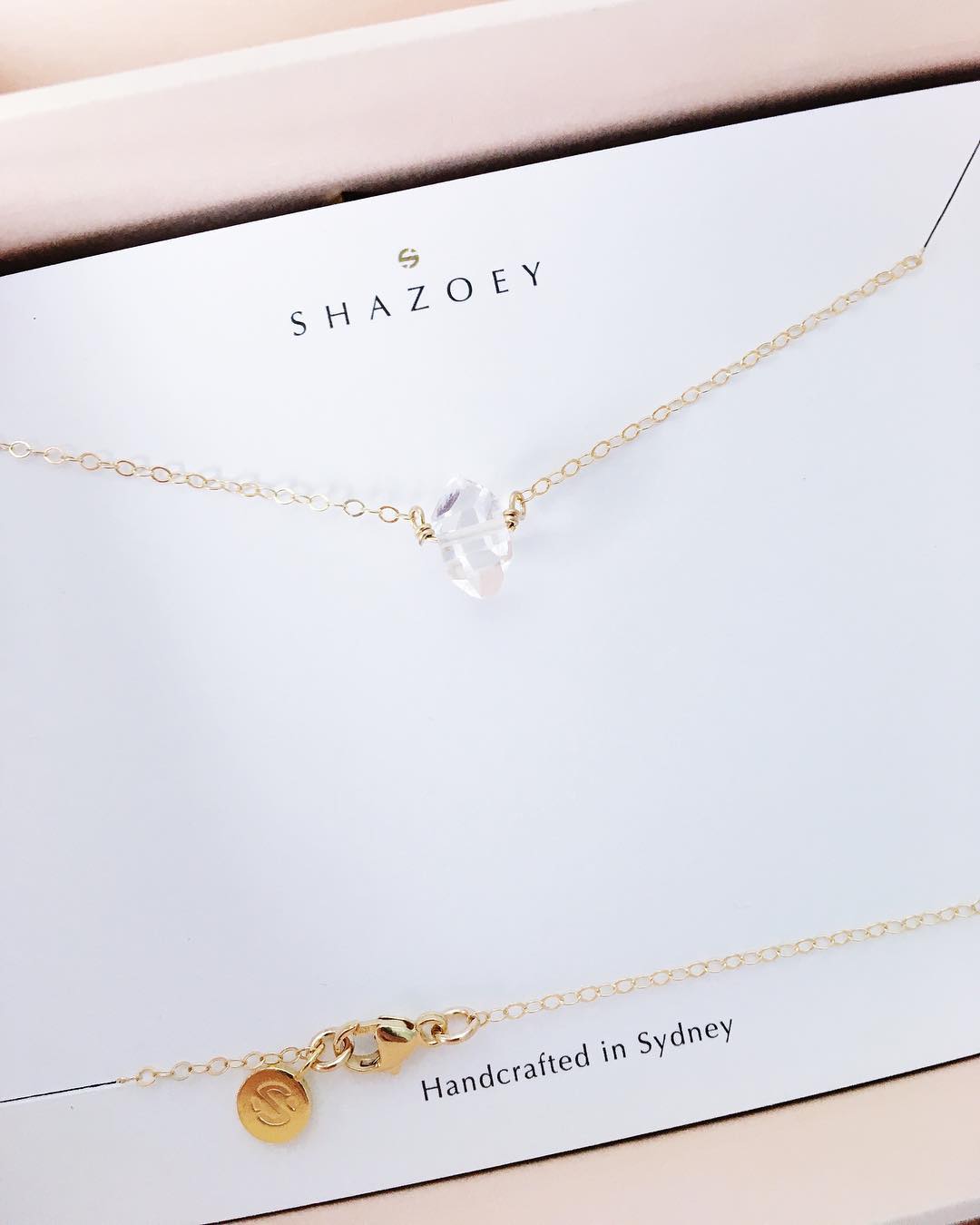 Gold necklace with a clear quartz point gemstone pendant on a Shazoey branded card.