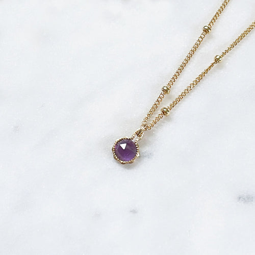 Round purple Amethyst necklace on a gold satellite chain on marble
