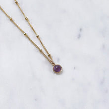 Purple amethyst birthstone pendant on a gold beaded necklace chain