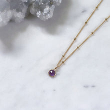 February birthstone pendant on a gold satellite chain next to a crystal quartz