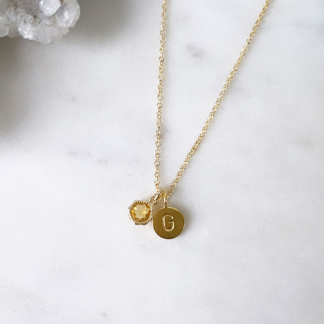 A sparkly round citrine pendant birth stone necklace with a letter initial charm on a fine gold cable chain