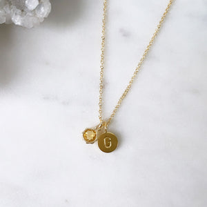 A round citrine pendant with a letter 'G' initial pendant on a fine gold cable chain