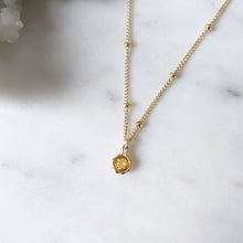 A faceted round orange citrine gemstone pendant hung on a satellite necklace chain