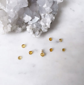 A round gold citrine pendant surrounded by citrine gemstones next to a quartz cluster on a marble board 