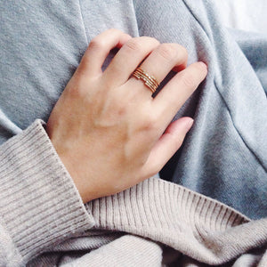 Gold filled dainty rings worn stacked, with hand resting on a brown woollen jumper