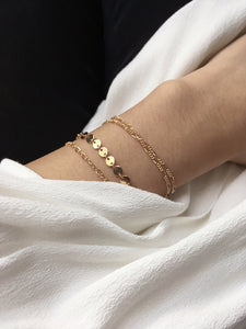 Hand wearing a gold figaro bracelet and dainty chain bracelets