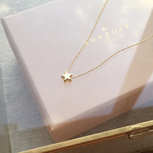 A tiny, dainty gold star strung on a delicate chain resting on top of a glass jewellery box