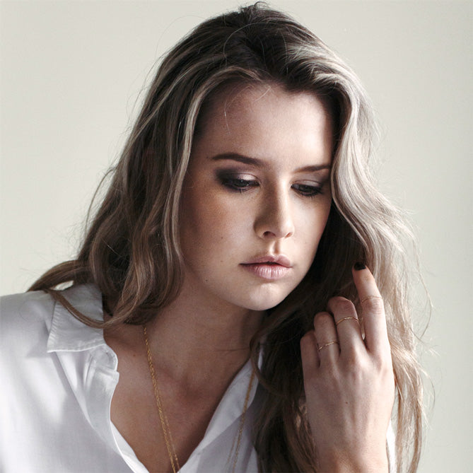 Model wearing thin dainty gold rings and fine gold chains