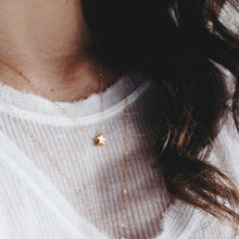A model with brown hair wearing a mini gold star necklace