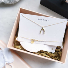 Gold wishbone charm necklace in pink box on marble table