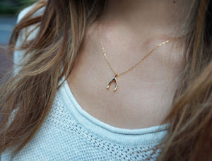 Woman with brown hair wearing a dainty gold wishbone necklace