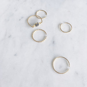 A collection of dainty fine gold rings, one with pavé set rough diamonds and others are open rings with a twisted and hammered finish