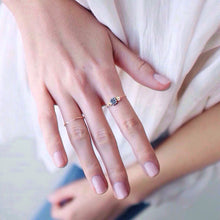 A hand wearing a raw diamond ring on the index finger with a thin gold band worn with a gold open twisted ring on the fourth finger