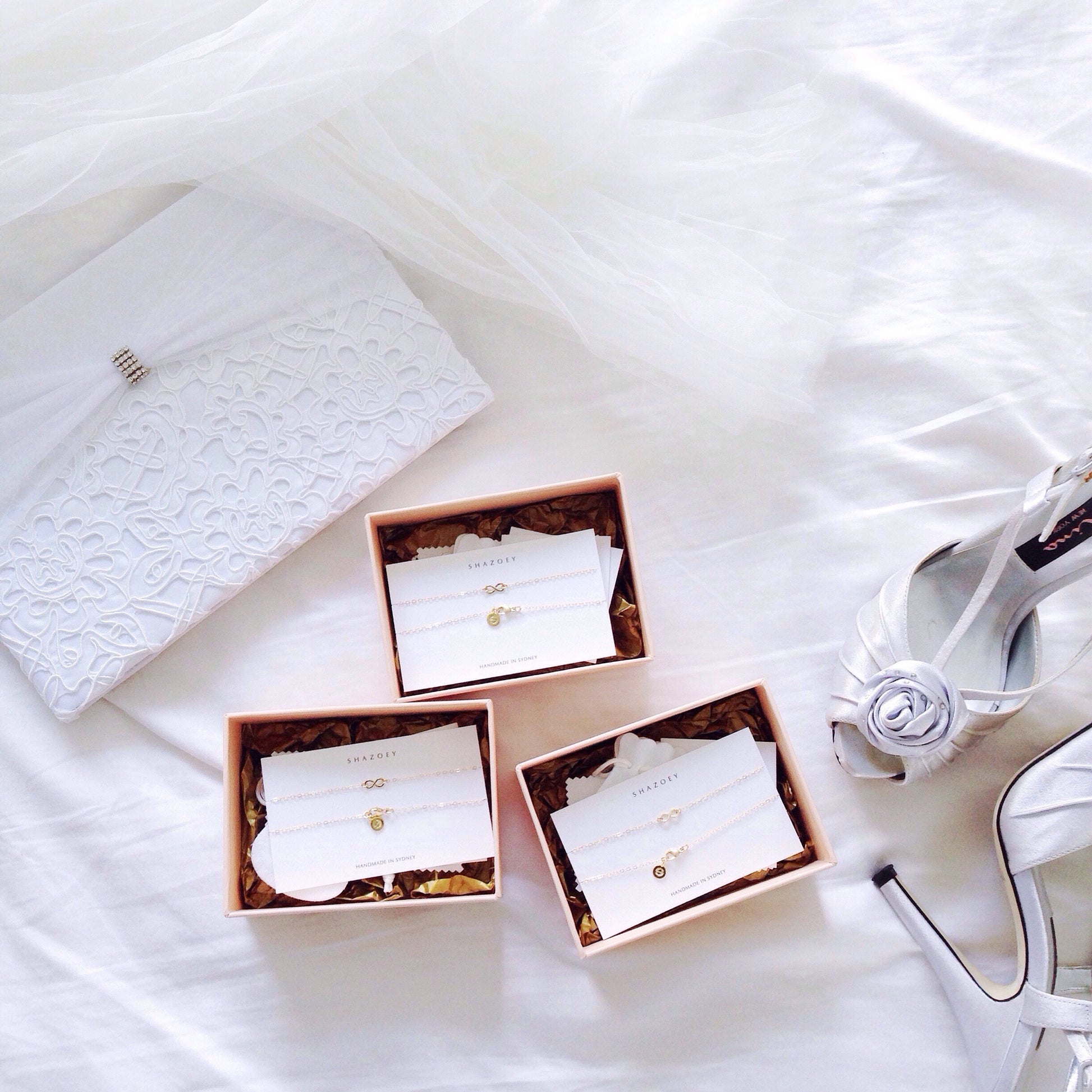 Bridesmaids jewellery of 3 infinity necklaces placed next to a wedding guestbook and bridal shoes