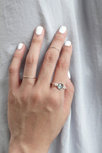 A hand model with white nail polish wearing thin sterling silver bands and a labradorite ring