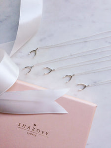 5 Sterling silver wishbone necklaces for a bridal party next to a white ribbon and pink box lid