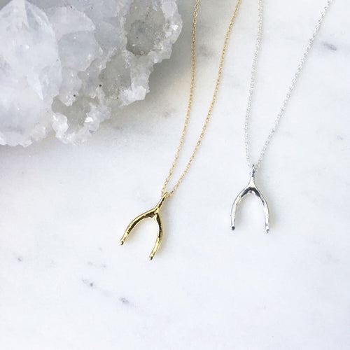 A dainty gold wishbone necklace placed next to a sterling silver minimalist wishbone necklace